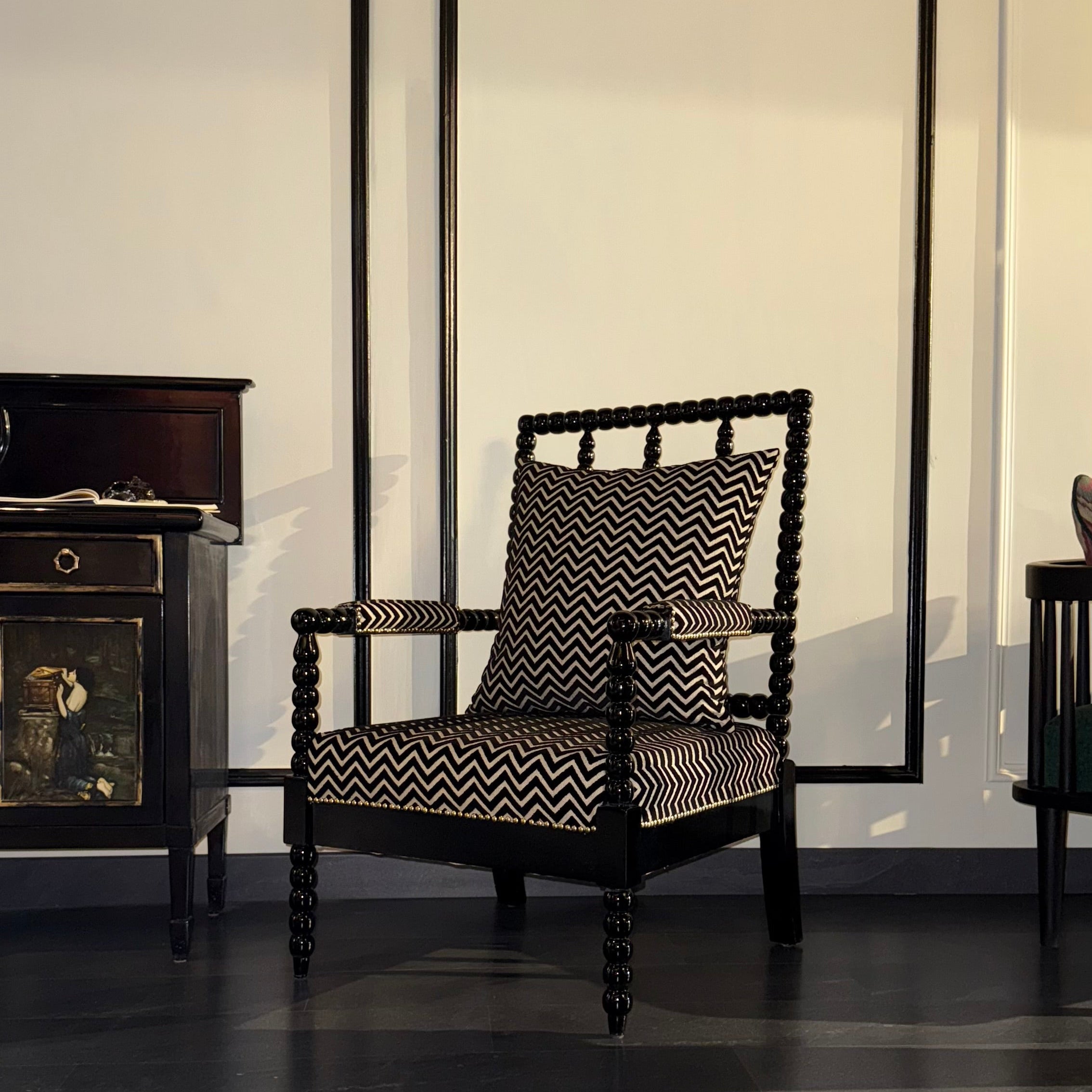 Dark wooden armchair with patterned cushion in a room with large mouldings on the wall.