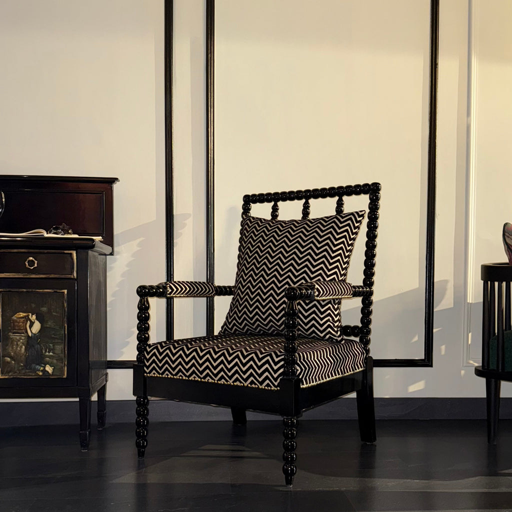 Dark wooden armchair with patterned cushion in a room with large mouldings on the wall.